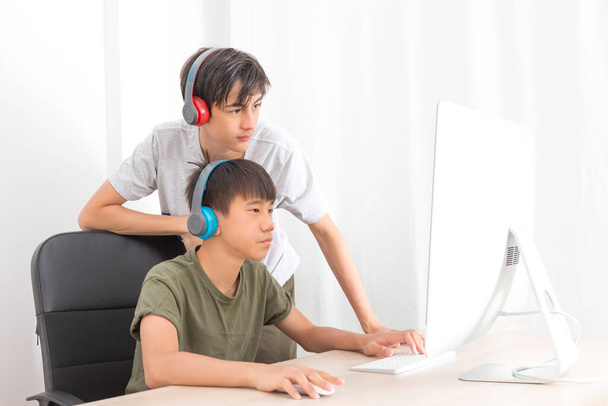 Kaksi teini-ikäistä poikaa kuulokkeilla tietokoneiden avulla pelata online-pelaamista kotona. Onnellinen aasialainen lapsi nauttia online-peli kotona. - Valokuva, kuva