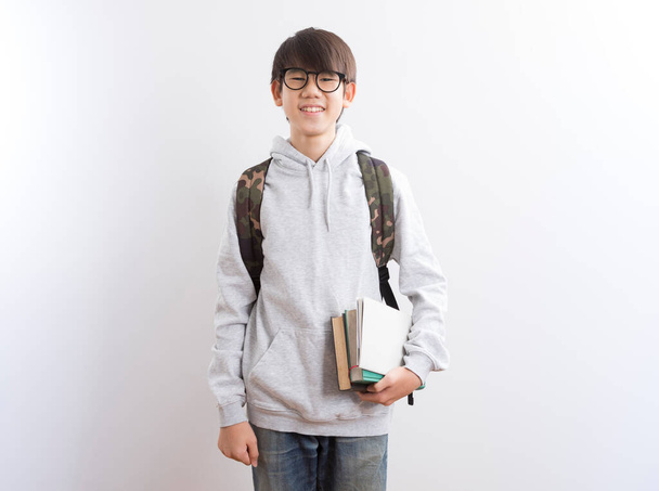 Asian teen boy students carrying a backpack and books pointing finger standing on white background. - Foto, afbeelding