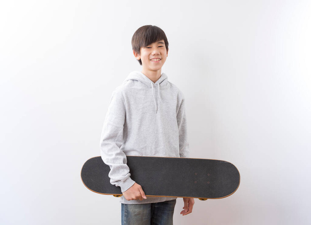 Asian teen boy holding skateboarding isolated on white background. - Фото, зображення