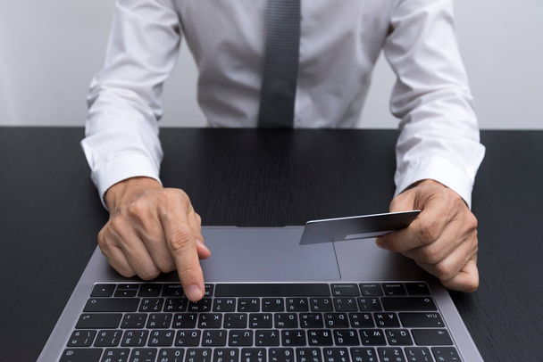 Zbliżenie dłoni dobrze ubranego mężczyzny w białej koszuli patrzącego na smartfona, korzystającego z laptopa na biurku. - Zdjęcie, obraz