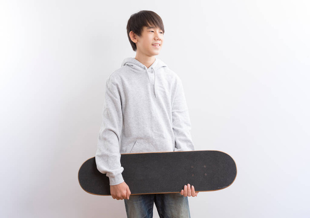 Asian teen boy holding skateboarding isolated on white background. - Фото, зображення