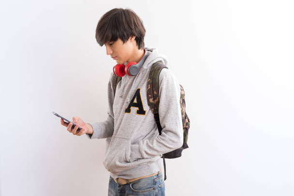 fiatal ázsiai fiú hátizsák és mobiltelefon elszigetelt fehér háttér - Fotó, kép