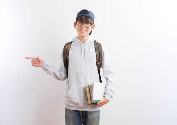 Asian teen boy students carrying a backpack and books pointing finger standing on white background. - Foto, imagen