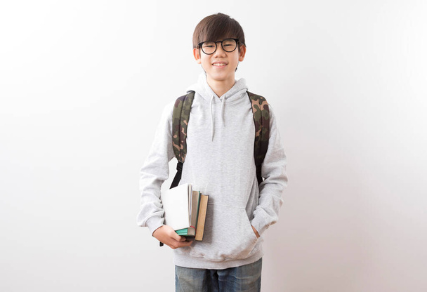 Ázsiai tini fiú diákok cipelnek egy hátizsák és könyvek ujjal mutogató álló fehér háttér. - Fotó, kép