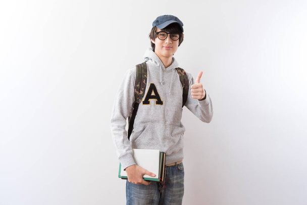 Handsome teen boy students carrying a backpack and books pointing finger standing on white background. - Zdjęcie, obraz
