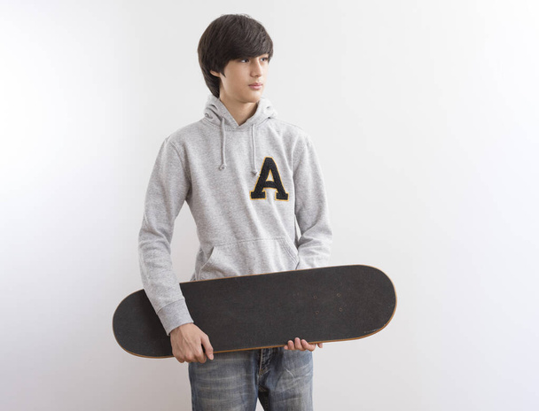όμορφος έφηβος αγόρι με skateboard σε λευκό φόντο. - Φωτογραφία, εικόνα