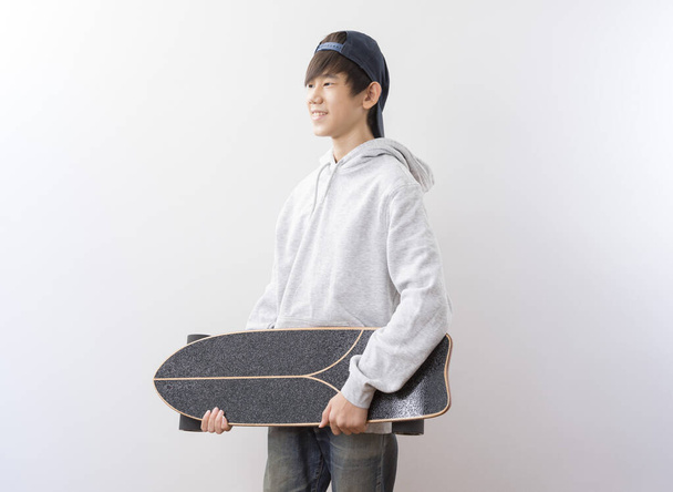 Asian teen boy holding longboard isolated on white background. - Фото, зображення