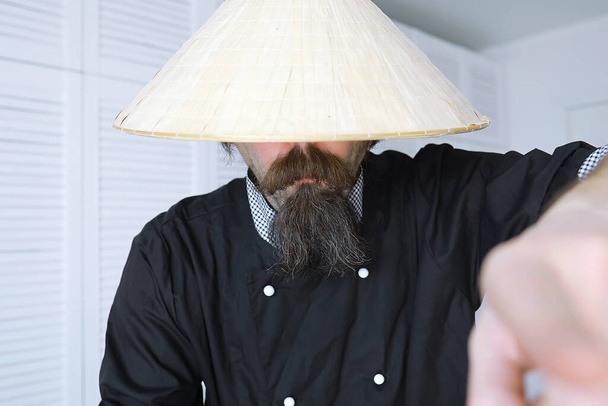 Zabawna parodia Azjaty w wietnamskim kapeluszu z brodą. Portret. azjatycki kucharz kawiarni. - Zdjęcie, obraz