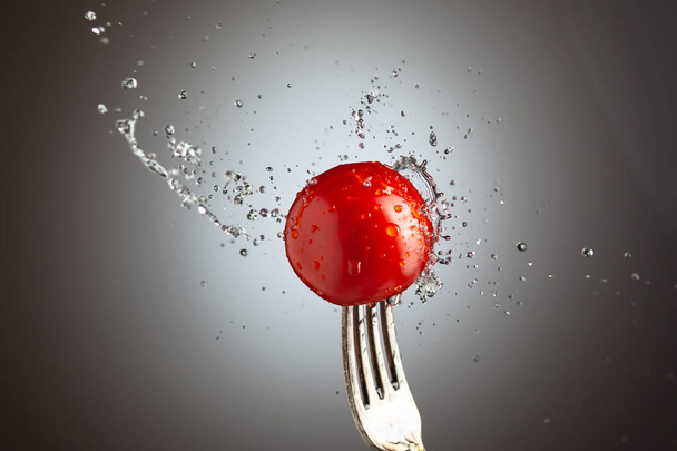 tomato cherry on a fork in splashes of water. Black white background - Photo, Image