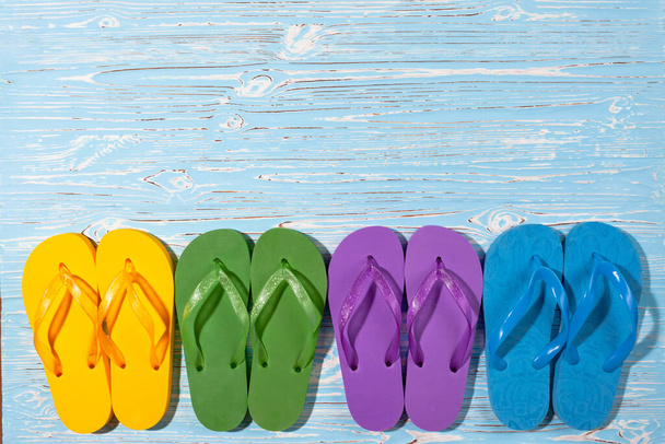 four pairs of multi-colored rubber beach flip flops on a blue wooden background, place under the text - Fotografie, Obrázek