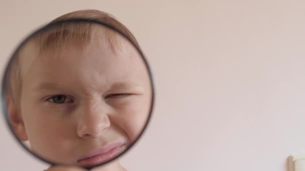 Primo piano maschio bambino che gioca con lente di ingrandimento zoom viso accigliato e occhiolino strofinando gli occhi - Filmati, video