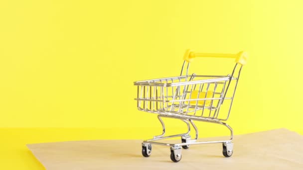 黄色の背景に空のショッピングカート、クローズアップ。ブラックフライデーショッピング&割引コンセプト - 映像、動画