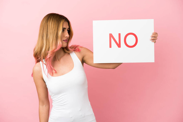 Young woman over isolated pink background holding a placard with text NO - Foto, imagen