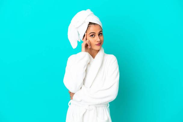 Young woman in a bathrobe over isolated blue background thinking an idea - Photo, Image