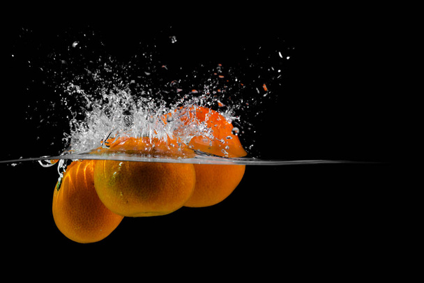 three tangerines fall into the water on a black background, copy space - Foto, Imagem