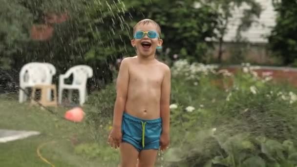 Lustiger Baby-Junge in Schutzbrille schreit Spaß unter fallenden Spritzwassertropfen - Filmmaterial, Video