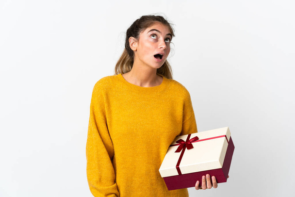 Young woman holding a gift isolated on white background looking up and with surprised expression - Photo, Image
