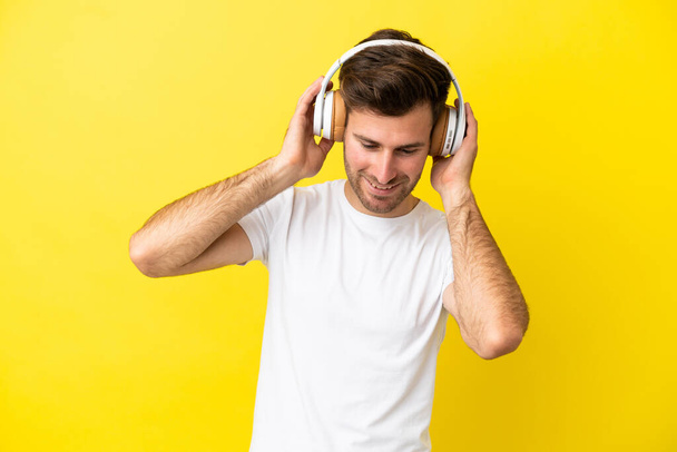 joven caucásico guapo hombre aislado en amarillo fondo escuchar música - Foto, Imagen