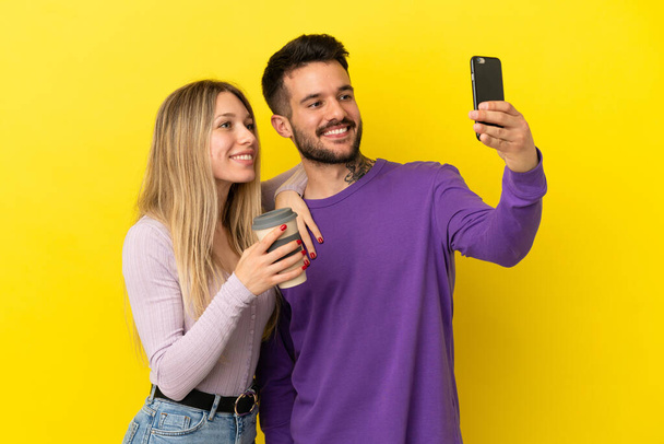 Casal jovem sobre fundo amarelo isolado fazendo uma selfie com o celular - Foto, Imagem