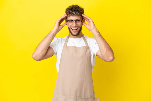 Restaurante camarero hombre rubio aislado sobre fondo amarillo con expresión sorpresa - Foto, Imagen