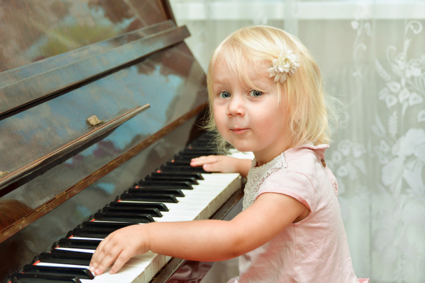 La petite fille près du piano sourit et regarde la caméra. Enseigner aux enfants dans une école de musique. - Photo, image