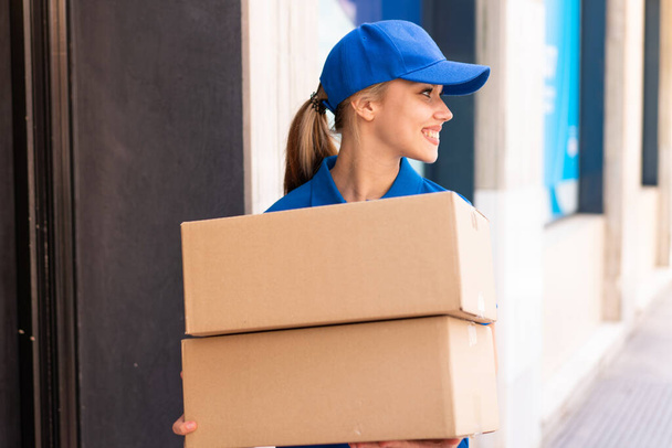 Young delivery woman at outdoors holding boxes with happy expression looking side - Photo, image