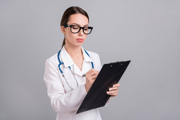 Photo of pretty confident young lady doctor workwear glasses writing prescription isolated grey color background - 写真・画像
