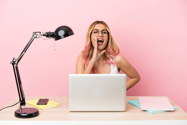 Молода студентка на робочому місці з ноутбуком над рожевим фоном кричить з відкритим ротом
 - Фото, зображення