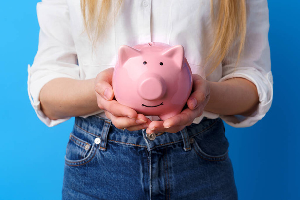 Female hands holding piggy bank moneybox against blue background - Foto, afbeelding
