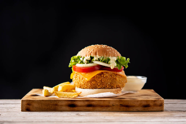 Ropogós csirkés burger sajttal és sült krumplival a fa asztalon - Fotó, kép