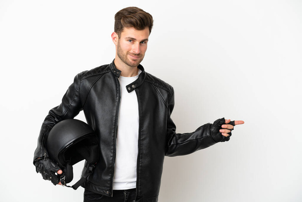 Jovem caucasiano com um capacete de motocicleta isolado no fundo branco apontando o dedo para o lado - Foto, Imagem