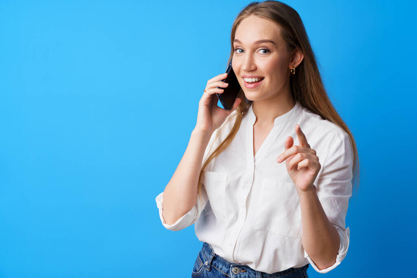 幸せな笑顔若い女性が青の背景に電話で話している - 写真・画像