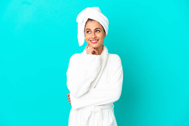 Young woman in a bathrobe over isolated blue background thinking an idea while looking up - Foto, afbeelding