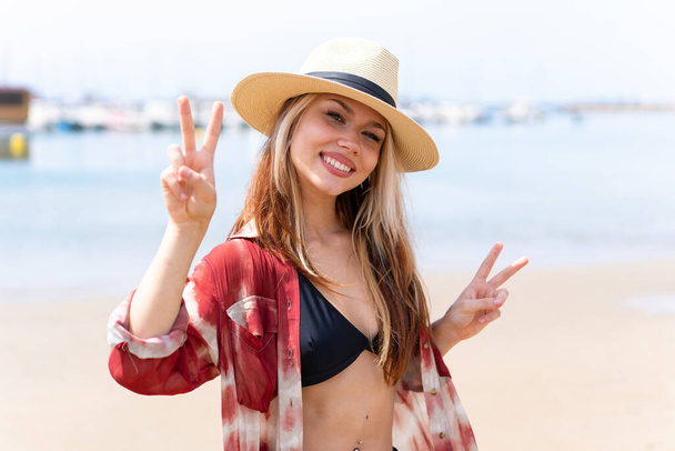 Yaz tatilinde kumsalda genç ve güzel bir kadın iki eliyle zafer işareti gösteriyor. - Fotoğraf, Görsel