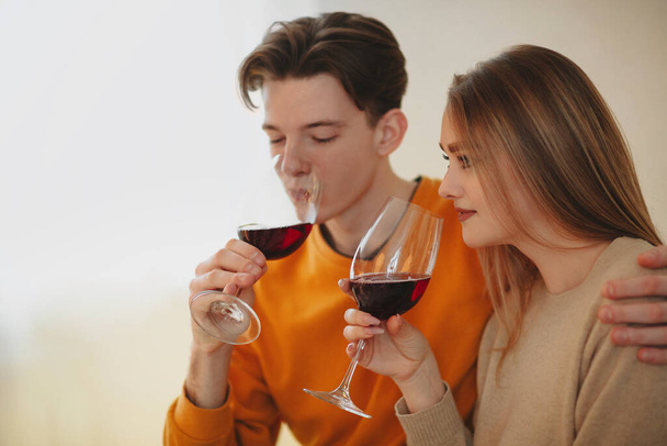Νεαρός άνδρας και γυναίκα αγκαλιάζει και απολαμβάνει το κόκκινο κρασί κατά τη διάρκεια ρομαντικό ραντεβού στο σπίτι - Φωτογραφία, εικόνα