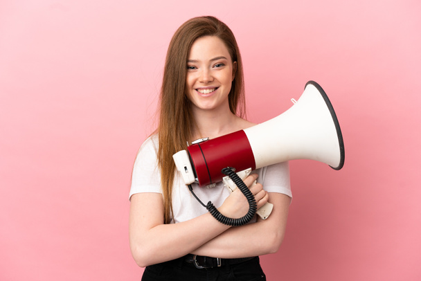 Teenager girl over isolated pink background holding a megaphone and smiling - Fotó, kép