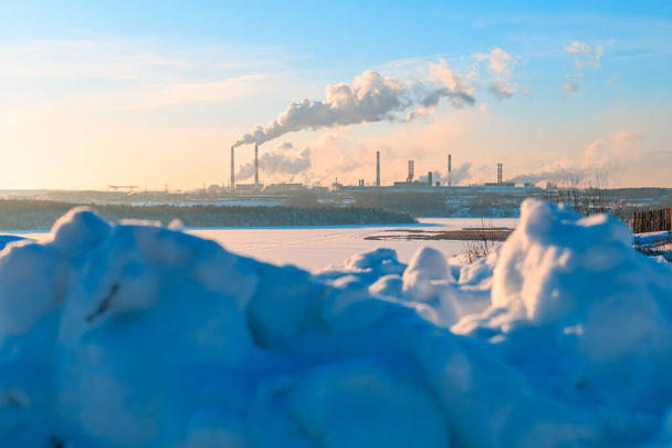前景には雪がたくさん積もっています背景には煙突がたくさんある蒸し工場です。環境汚染です - 写真・画像
