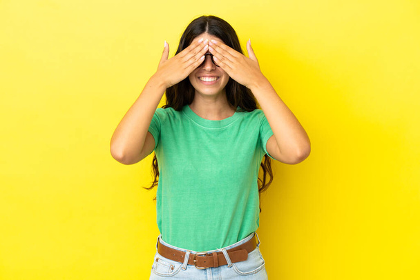 Young caucasian woman isolated on yellow background covering eyes by hands and smiling - Foto, immagini