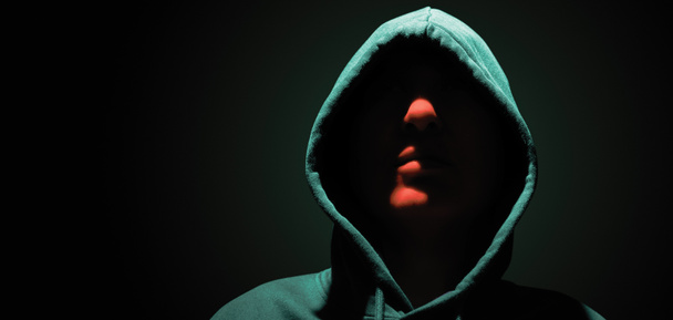 Portrait of a man with a hidden face in a hood on a dark background. - Foto, imagen