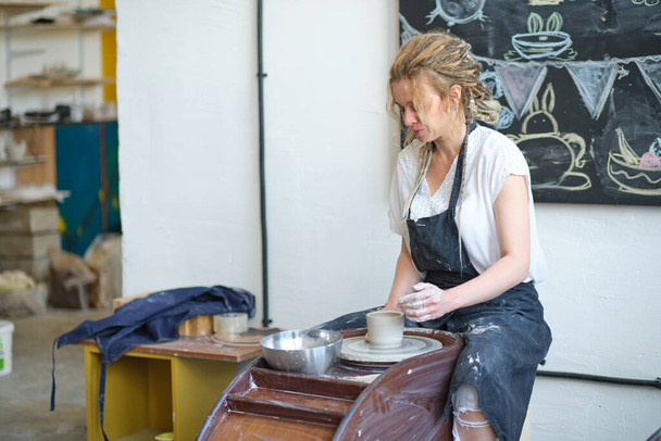 Kapalı kadın elleri kilden yemek yapar. Kadın elleri çömlekçi çarkında çalışıyor. Usta çömlekçi bir atölyede çalışıyor. - Fotoğraf, Görsel