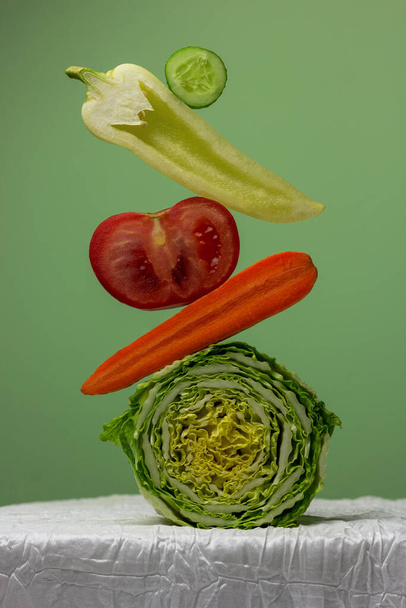 Капуста, помидор, перец, огурец, морковь на зеленом фоне. Концептуальный творческий натюрморт с балансировкой овощей. Копировать бумажную карту. - Фото, изображение