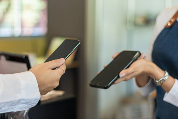 Eine Frau nutzt eine App auf ihrem Smartphone, um Kaffee am Coffeeshop-Tresen zu scannen und zu bezahlen, weil es bequem ist.Concept Scan, um Waren mit digitaler Brieftasche oder Internet-Banking zu bezahlen - Foto, Bild