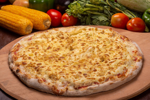 Pizza au poulet et mozzarella sur une planche en bois et légumes en arrière-plan. - Photo, image