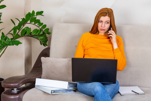 Female freelancer talking by phone and working on laptop at home - Foto, afbeelding