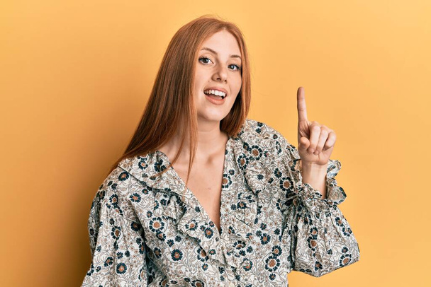 Νεαρή Ιρλανδή γυναίκα που φοράει καθημερινά ρούχα χαμογελώντας με μια ιδέα ή ερώτηση δείχνοντας το δάχτυλο με χαρούμενο πρόσωπο, νούμερο ένα  - Φωτογραφία, εικόνα