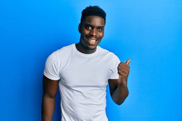 Knappe zwarte man draagt casual witte t-shirt duim wijzen naar de zijkant glimlachen blij met open mond  - Foto, afbeelding
