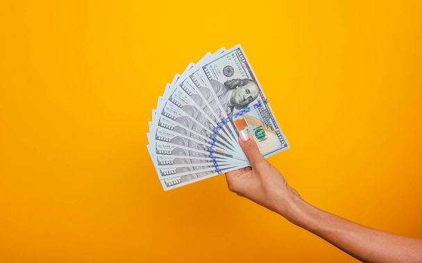 Close up photo of beautiful female hands holding the bunch of dollars of USA isolated on yellow background. Economy, business and finance concept - Valokuva, kuva