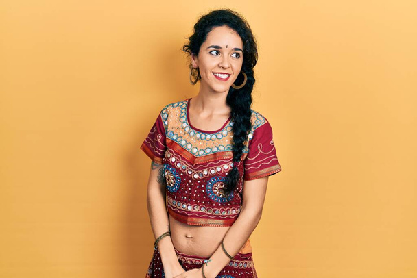 Jovem mulher vestindo roupas bindi e bollywood olhando para o lado com sorriso no rosto, expressão natural. rindo confiante.  - Foto, Imagem