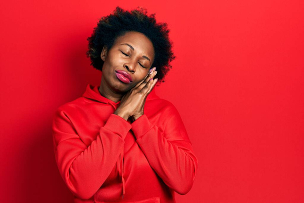Молода афроамериканська жінка у звичайній светрі спить втомлений сон і позує руками, посміхаючись закритими очима..  - Фото, зображення