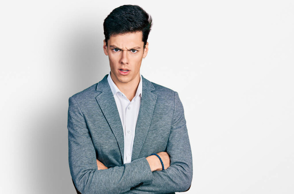 Young hispanic business man with arms crossed gesture in shock face, looking skeptical and sarcastic, surprised with open mouth  - Фото, изображение